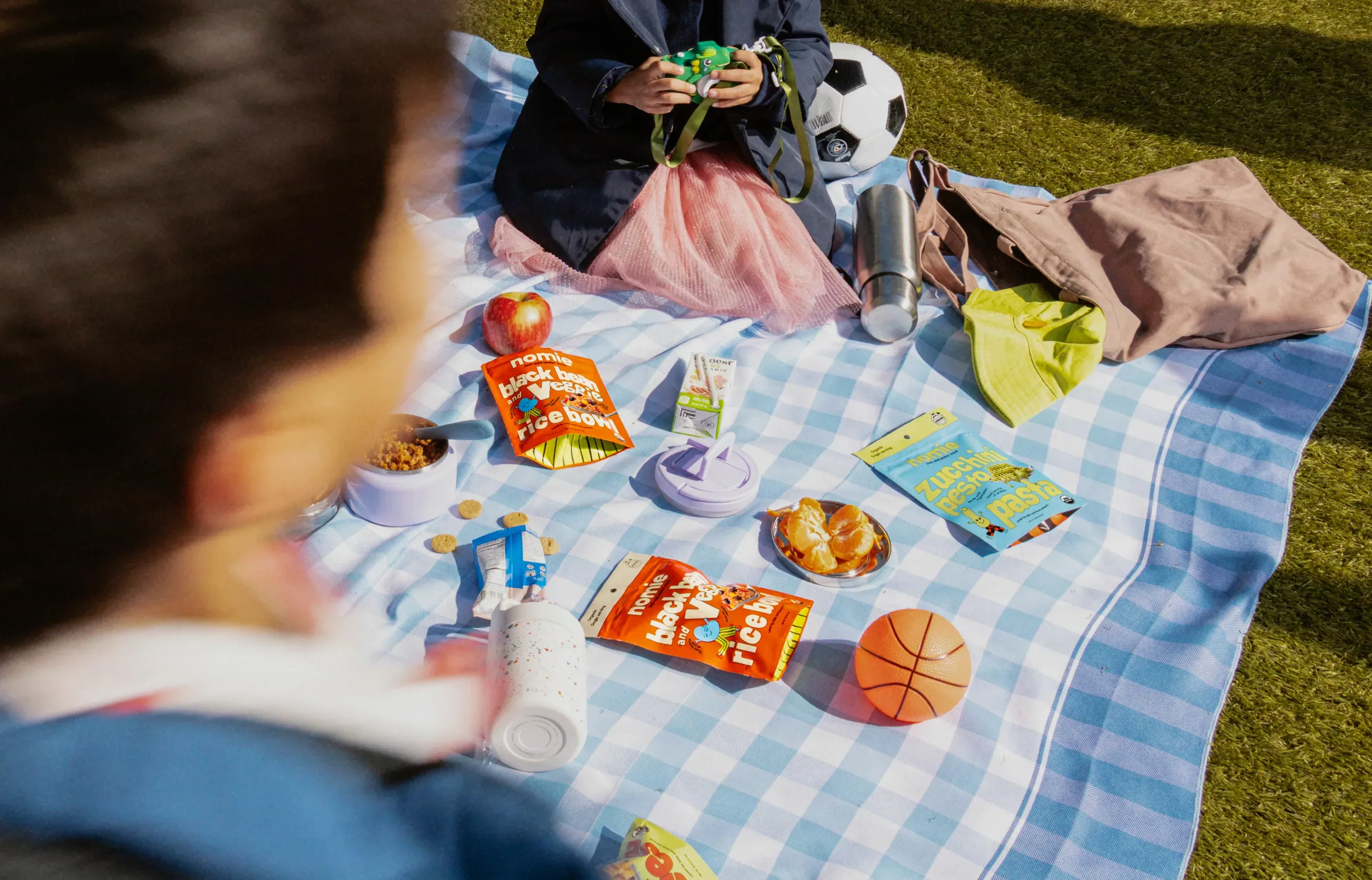 Children at a picnic with Nomie pouches on a blue checked blanket