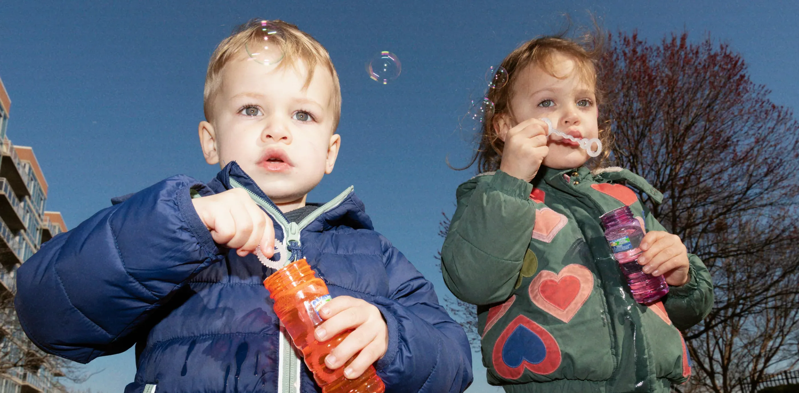 Two children blowing bubbles outdoors, one holding a Nomie drink