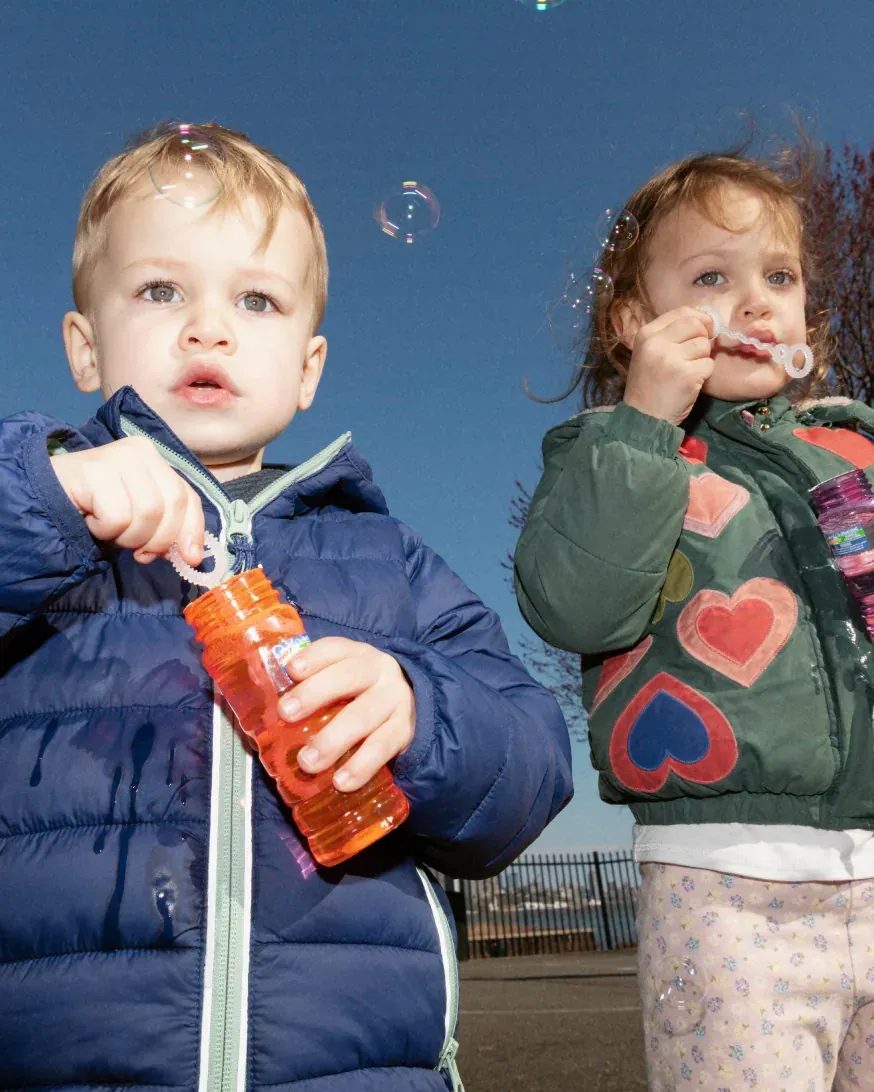 Two children outdoors, one holding a Nomie drink